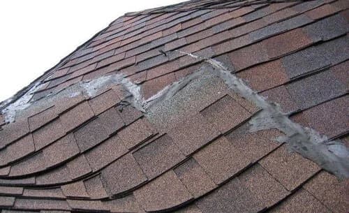 A worn shingle roof valley with sloppy patched sealant and lifting shingles.