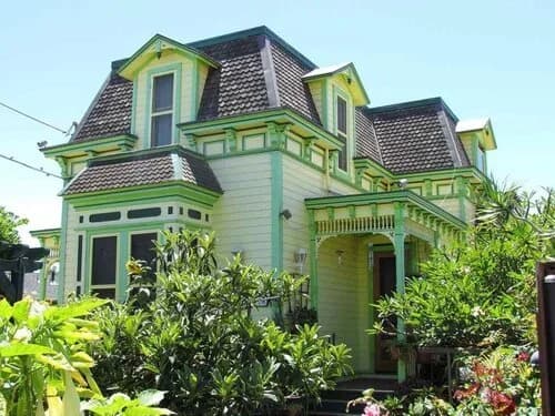 A green and yellow Victorian house with a mansard-style tile roof and dormers.