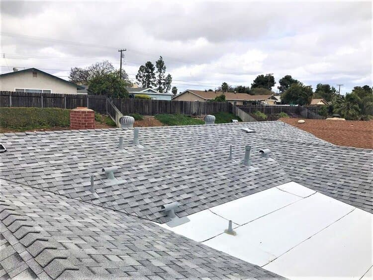 A gray shingle roof fitted with multiple metal pipe vents and turbine vents.