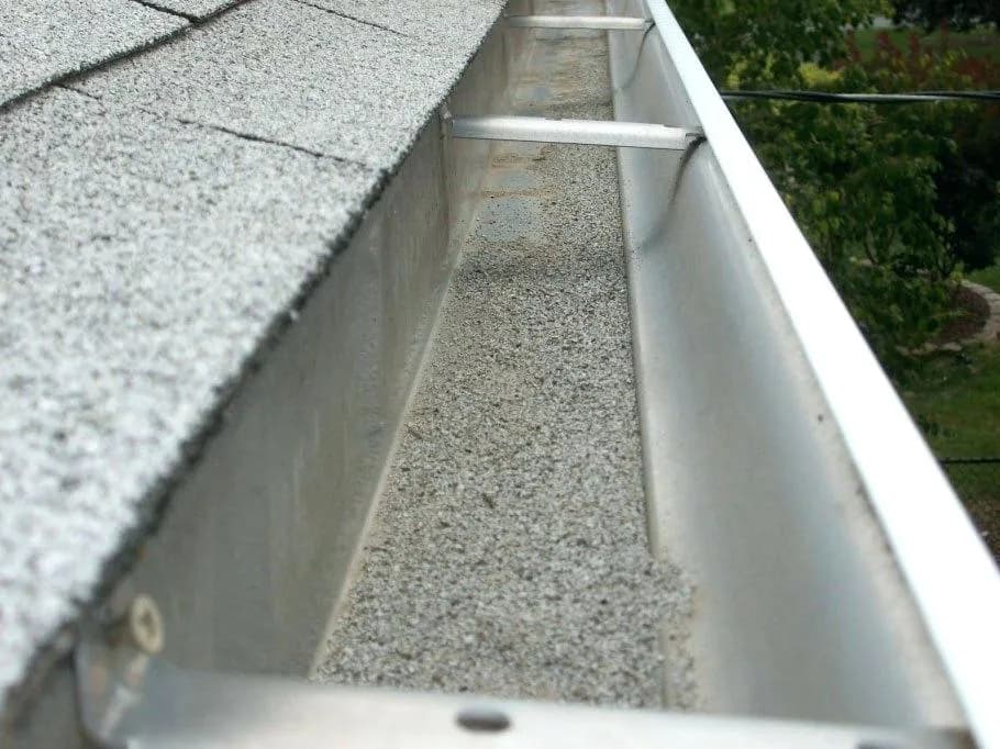 A rain gutter filled with gray shingle granules and debris.