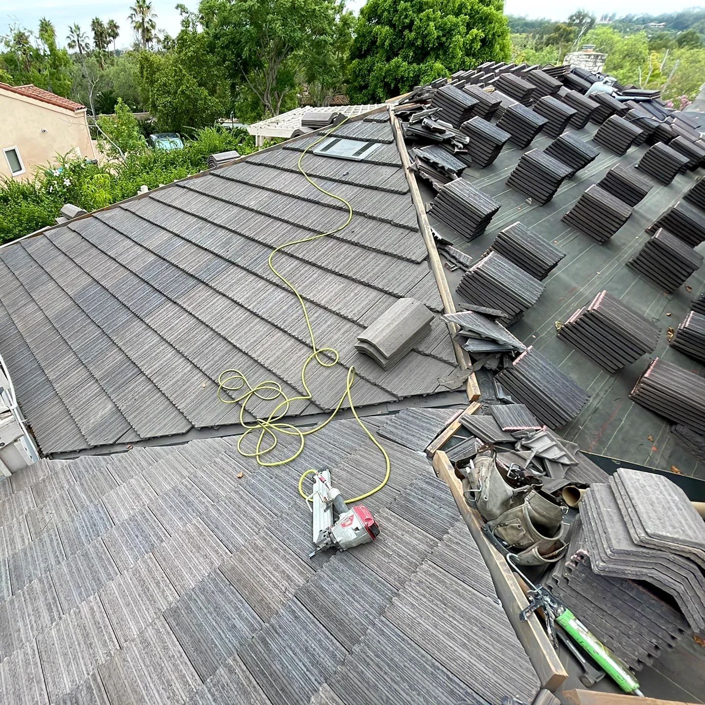 Concrete tiles stacked on a roof mid-replacement with exposed underlayment and tools.
