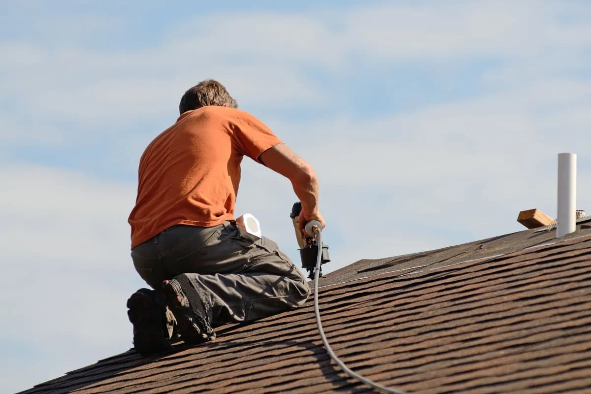 A roofing worker in a tool belt standing beside a layered roof edge during a job.