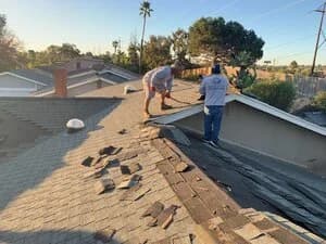 Two workers tearing off old shingles during a roof replacement.