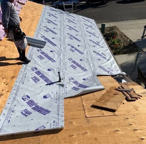 A roofer installing synthetic underlayment over a plywood roof deck on a San Diego home.