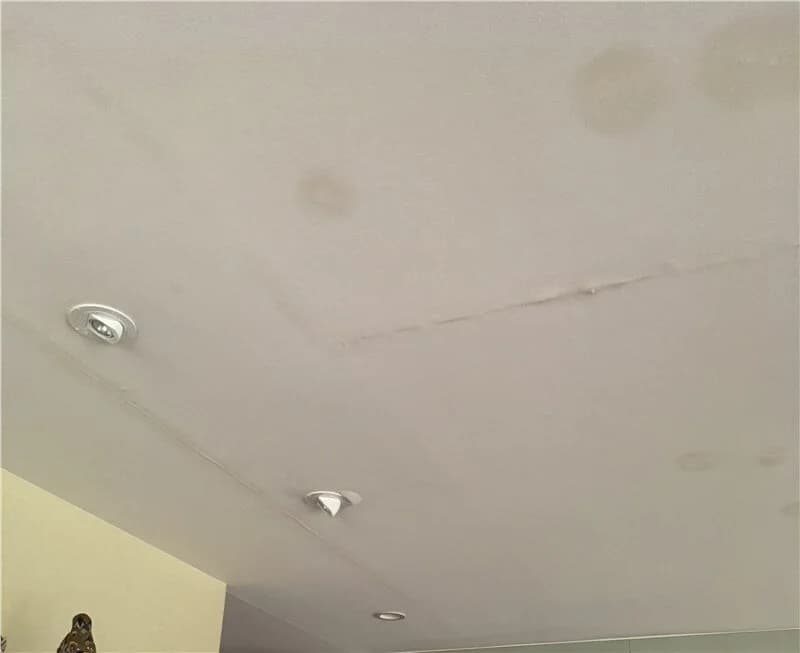 An interior white ceiling with multiple brown water stains and discoloration around recessed light fixtures from a leak.