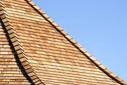 A curved cedar wood-shake shingle roof against a clear blue sky.