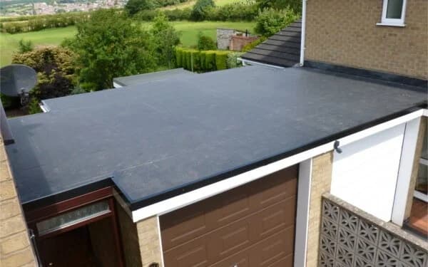 A flat black EPDM rubber membrane roof over an attached garage with a green hillside behind.