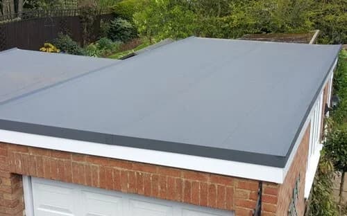 A close-up aerial view of a flat gray GRP fibreglass roof on a brick garage with a white fascia edge.