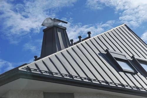 Step and counterflashing tucked against masonry on a metal-paneled roof.