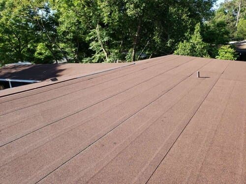 A low-slope roof section beside the main roof, framed by trees.