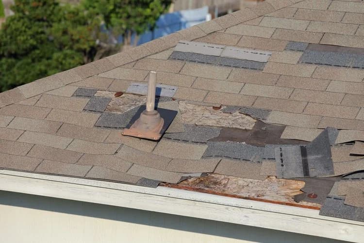 A close-up of a shingle roof around a vent pipe with rotted decking and crude patch repairs.