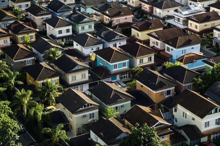 Aerial view over a dense neighborhood of houses with dark tile roofs surrounded by greenery.