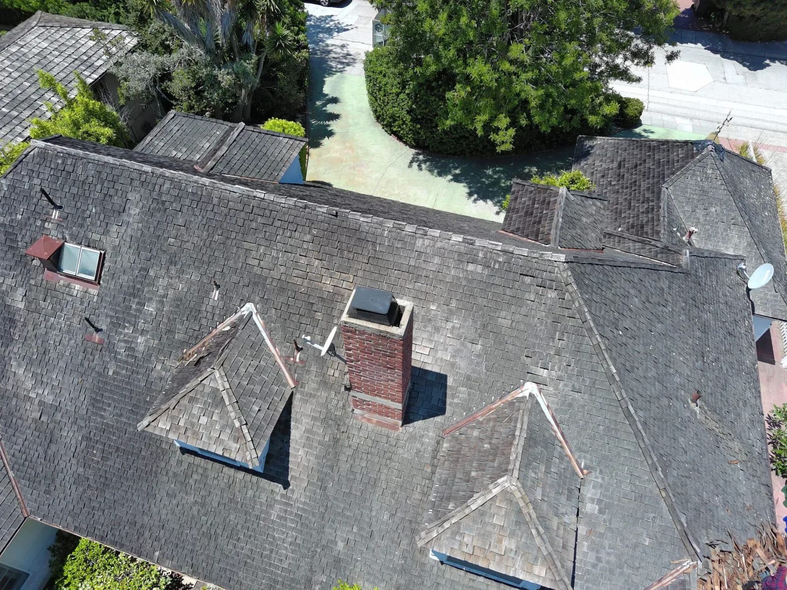 Aerial view of a large gray asphalt shingle roof with a brick chimney and dormers.