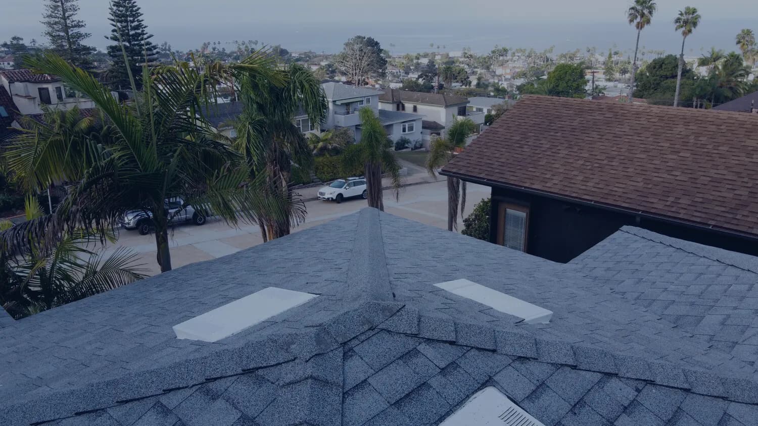 A roofer's view down a shingle roof ridge over a coastal neighborhood.