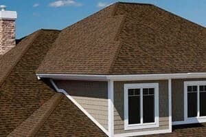 A neat brown asphalt shingle hip roof on a residential home with white-trimmed gables and gutters.
