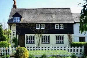A white English cottage with a steep tiled roof and dormer windows.