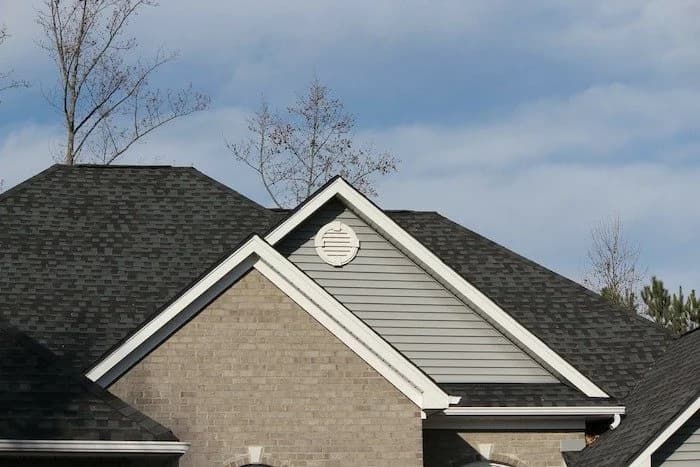 Peaked gable rooflines of a brick home with dark shingles and a round gable vent.