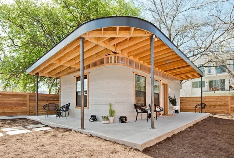 A modern home with a curved metal roof and exposed wood beams over a covered patio.