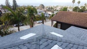 A newly installed gray asphalt shingle roof ridge overlooking a coastal residential neighborhood.