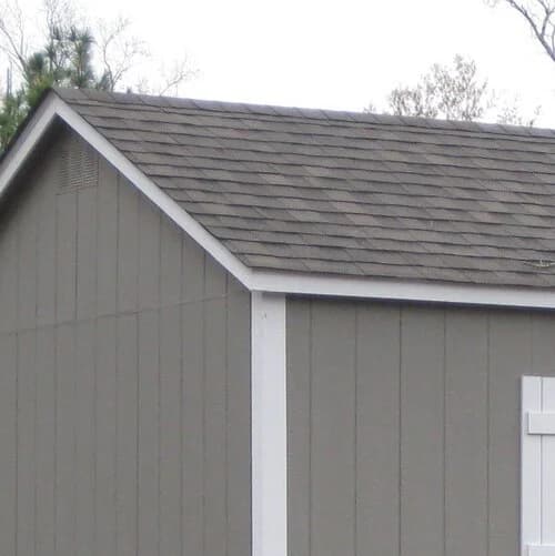 The gable end of a gray shed showing an asphalt shingle roof, white trim, and a small vent.