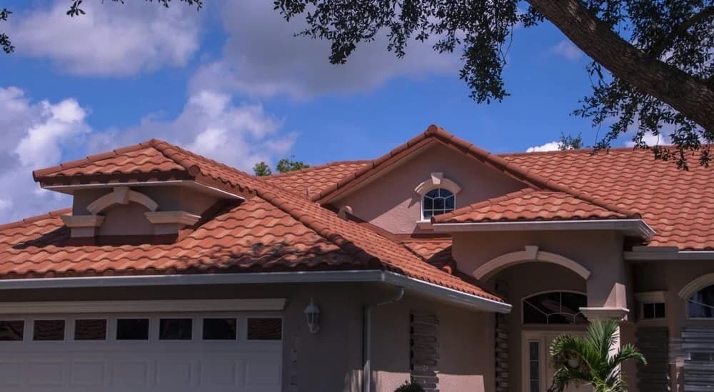 A home with a terracotta barrel-tile roof and dormers under a partly cloudy sky.