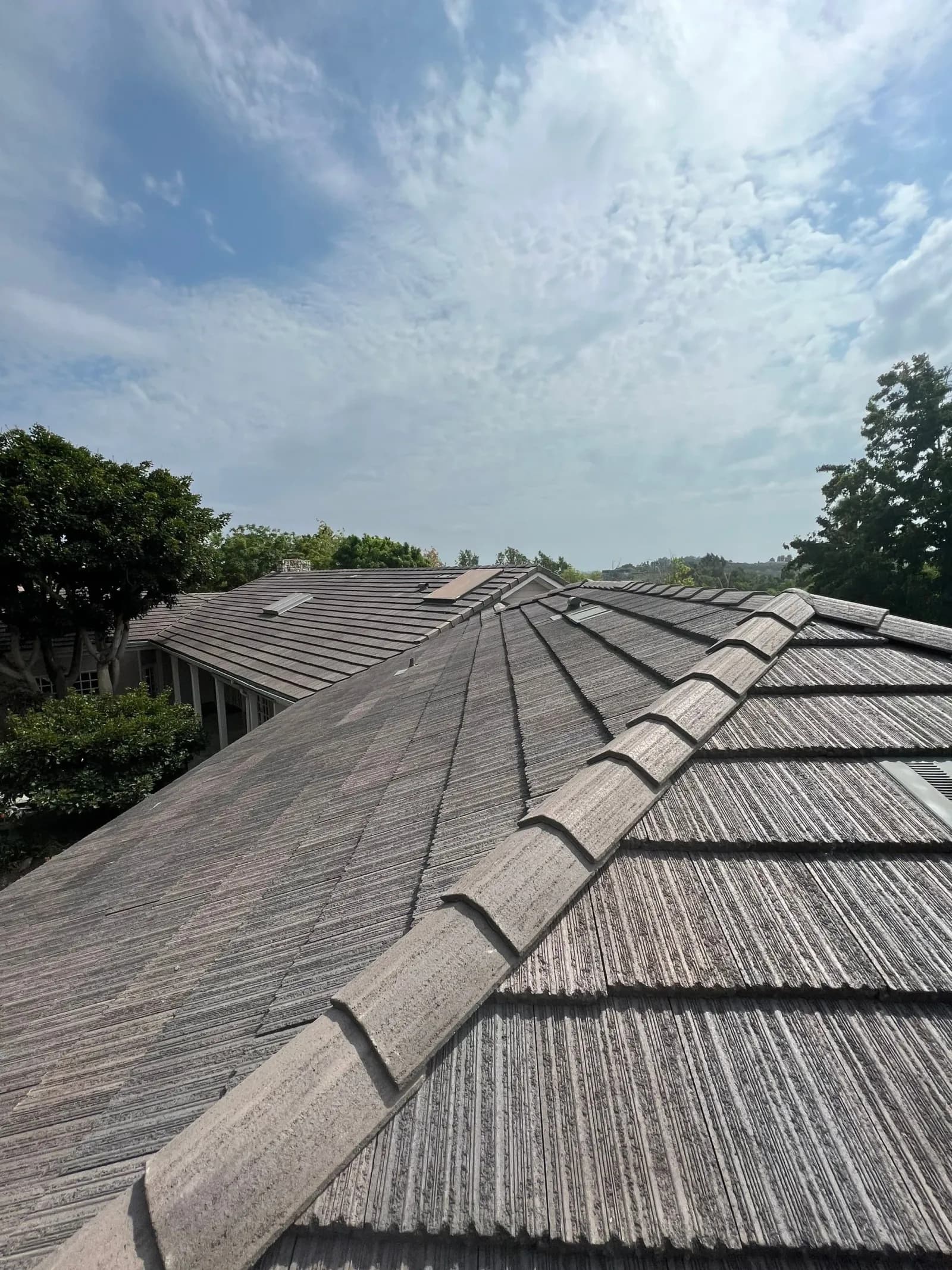 Looking up the ridge line of a weathered gray tile roof against a partly cloudy sky.