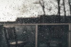 Rain droplets running down a window pane with a blurred, gloomy view of a building and trees outside.