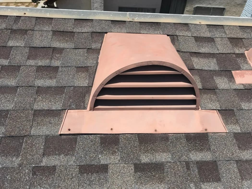 A copper louvered dormer-style roof vent set into a brown shingle roof.