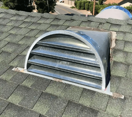 A galvanized half-round louvered Vulcan dormer vent installed on a gray asphalt shingle roof.